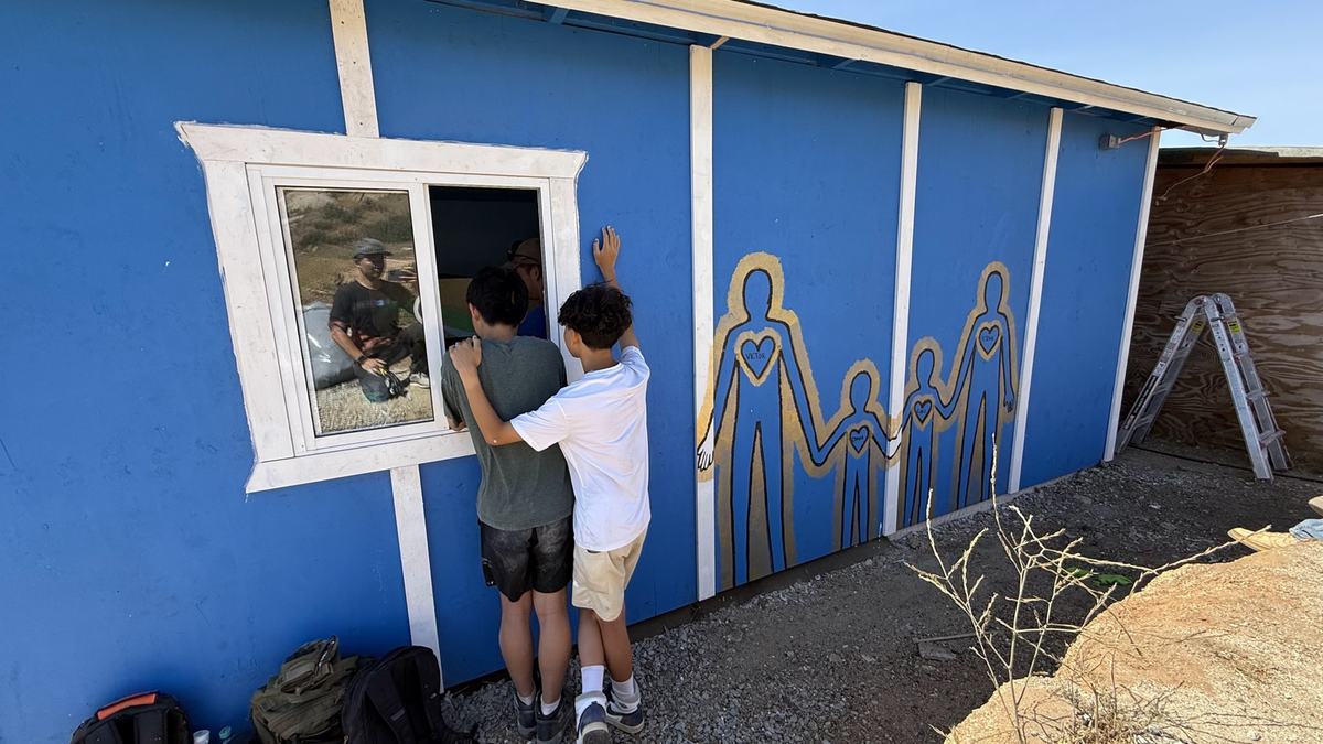 Children painting a family mural on the wall of a new blue home